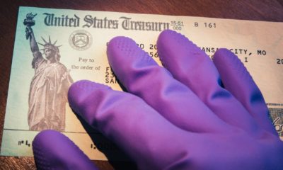 United States Treasury check being held by rubber glove illustrates US Government coronavirus economic impact payment sent-Second Stimulus Check-ss-Featured