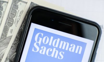 Logo of the Goldman Sachs Group in the smartphone lying on paper with charts and one hundred dollar bills-Goldman Sachs Advice-ss-featured