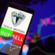 Company logo Tesla Motors on smartphone screen hand of trader holding mobile phone showing BUY or SELL on background of stock chart-Tesla Joins S&P 500-ss-featured
