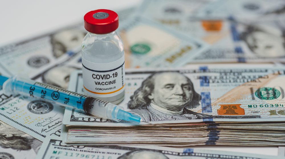 conceptual vial of coronavirus or covid-19 vaccine on a stack of US one hundred dollar bills next to a syringe and more banknotes-Coronavirus Vaccines Cost-ss-featured