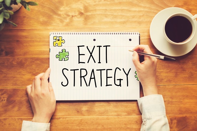 Exit Strategy text with a person holding a pen on a wooden desk-exit-ss