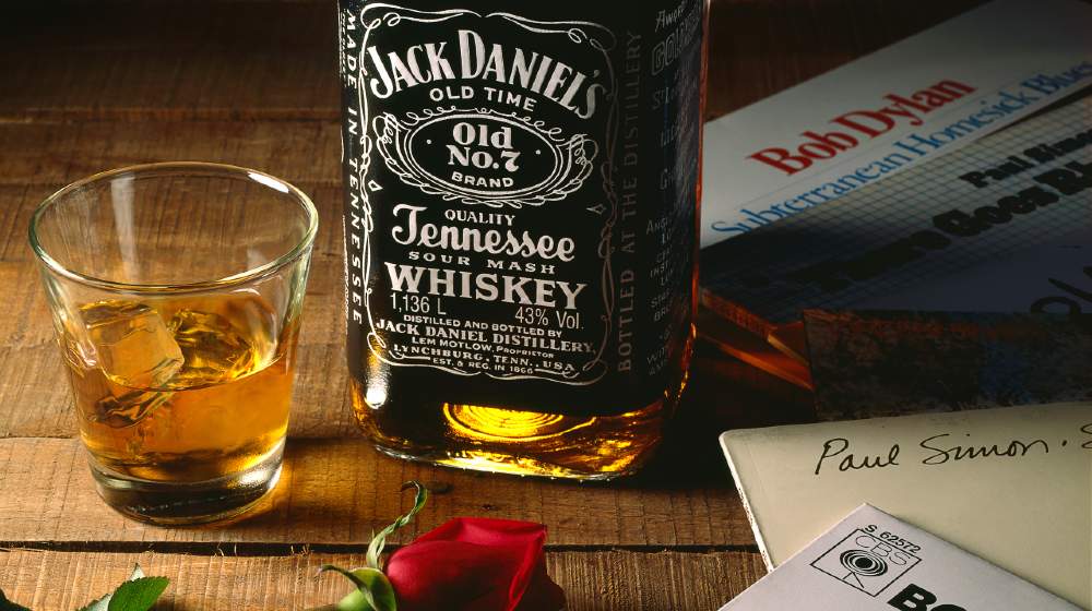 Jack Daniels bottle with a rose, a glass of whiskey and some LP records on wooden surface-US Whiskey Tariffs-ss-featured