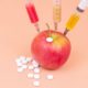 Syringes with different chemicals injections and tablets in a red apple on an orange background | How COVID-19 Impacting AI for Drug Discovery Market | Featured