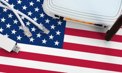 United States of America flag depicted on table with internet rj45 cable, wireless usb wifi adapter and router | Big Tech Wary Of Biden’s $100B ‘Broadband for All’ Plan | Featured