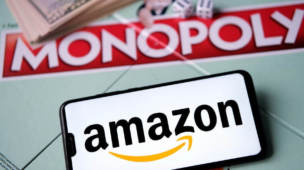 Amazon logo on smartphone placed next to Monopoly game with real money | Washington DC Sues Amazon For Monopoly Practices | Featured