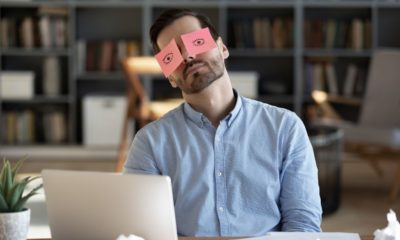 Exhausted tired businessman with painted eyes on stickers, adhesive notes on face sleeping at workplace | Burned out millennials quitting their jobs eye 'private money flowing around’ | Featured