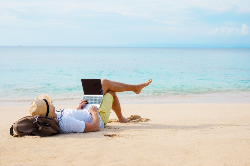 Man working on laptop computer while relaxing on the beach | The Way to Financial Freedom and Independence