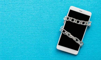 White smartphone with metal chain on blue background. Digital detox, dependency on tech, no gadget and devices | DeSantis Sign New Law Against Deplatforming Candidates | Featured