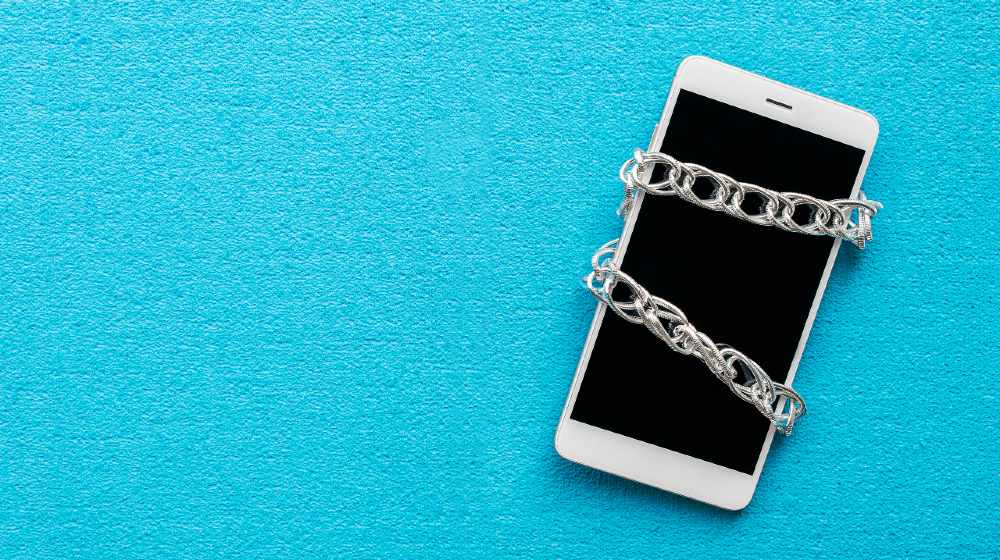 White smartphone with metal chain on blue background. Digital detox, dependency on tech, no gadget and devices | DeSantis Sign New Law Against Deplatforming Candidates | Featured