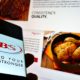 Person holding cellphone with logo of Brazilian meet processing company JBS S.A. on display with website | Cyberattack Hits World’s Largest Meat Supplier | Featured