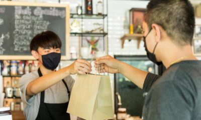 Social distance conceptual waiter giving takeaway bag to customer at cafe | When Getting Back to 'Normal' Doesn't Make Sense | featured