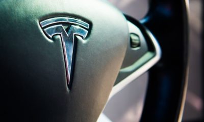 Tesla logo on black leather luxury electro mobile car steering wheel | Tesla Recalls Vehicles Over Seat Belt Safety Issues | featured