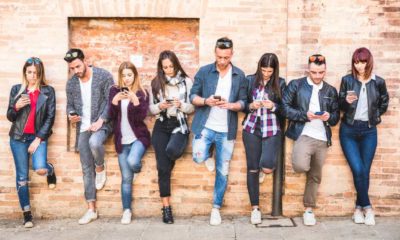 Friends group using smartphone against wall at university college backyard break | Tech firms in new battle for millennials | featured