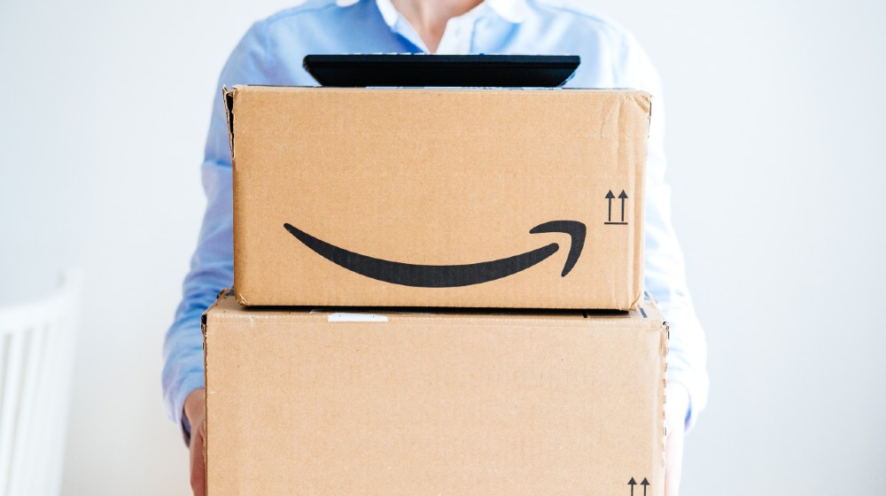 Vie from the front of happy smiling woman holding two large Amazon Prime cardboard | The Challenges Facing New Amazon CEO Andy Jassy | featured