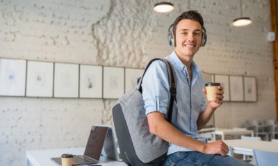young handsome man sitting on table in headphones with backpack in co-working office | Walmart Offers Workers Free College Tuition And Books | featured