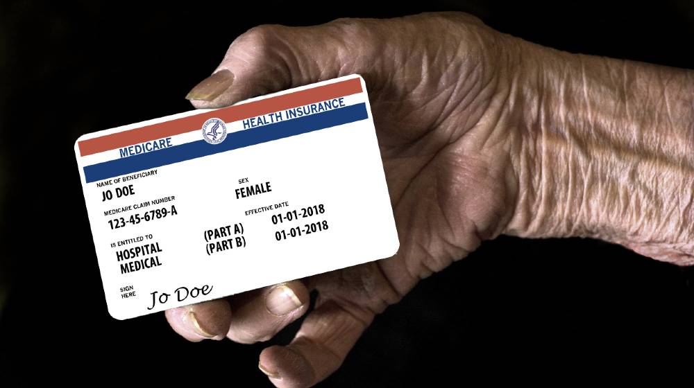An elderly female hand holds a mock United State government Medicare Health Insurance card | Democrats’ $3.5T Budget Plan Includes Expanded Medicare | featured