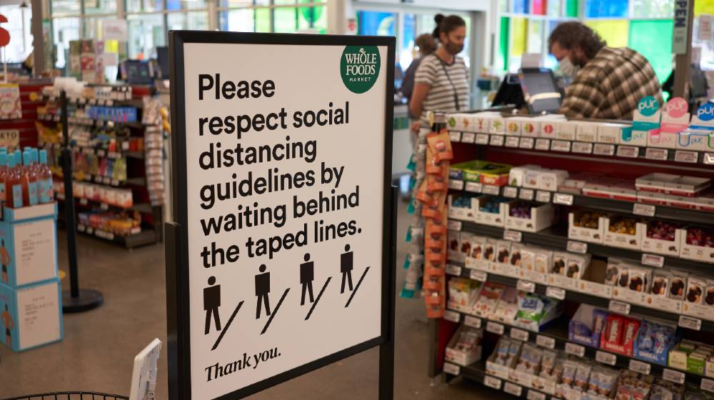 The-sign-at-the-checkout-lane-in-a-Whole-Foods-Market-reminds-shoppers-to-respect-social-distancing-guidelines | Businesses Struggle With Shifting COVID-19 Guidelines | featured