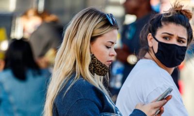 Young long hair blonde woman texting and walking with face mask down and mother friend looking back frustrated during covid-19 coronavirus pandemic | More Workers Support Heavier Penalties for Unvaccinated Ones | featured