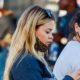 Young long hair blonde woman texting and walking with face mask down and mother friend looking back frustrated during covid-19 coronavirus pandemic | More Workers Support Heavier Penalties for Unvaccinated Ones | featured