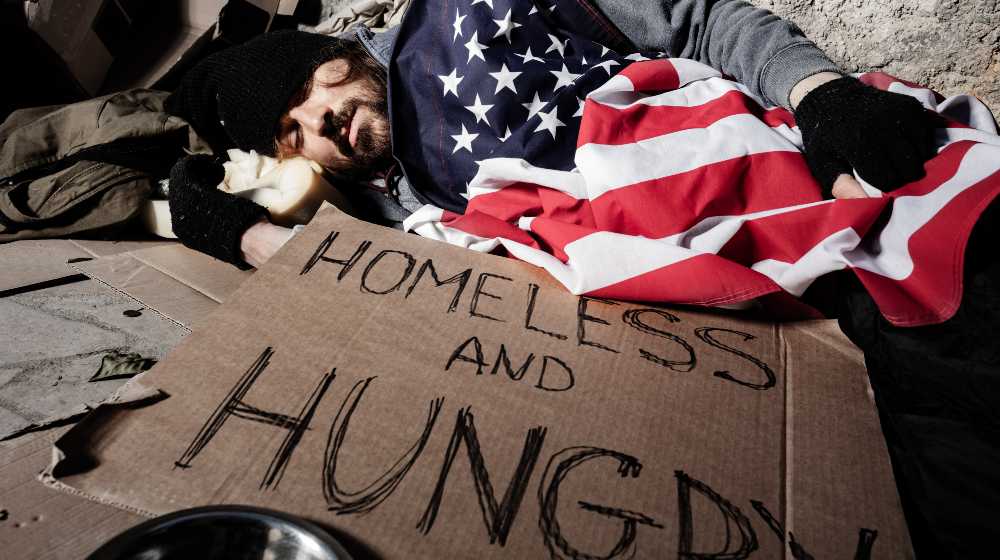Homeless man sleeping outsie under American flag | COVID-19 Pushed 31 Million People Into Dire Poverty | featured