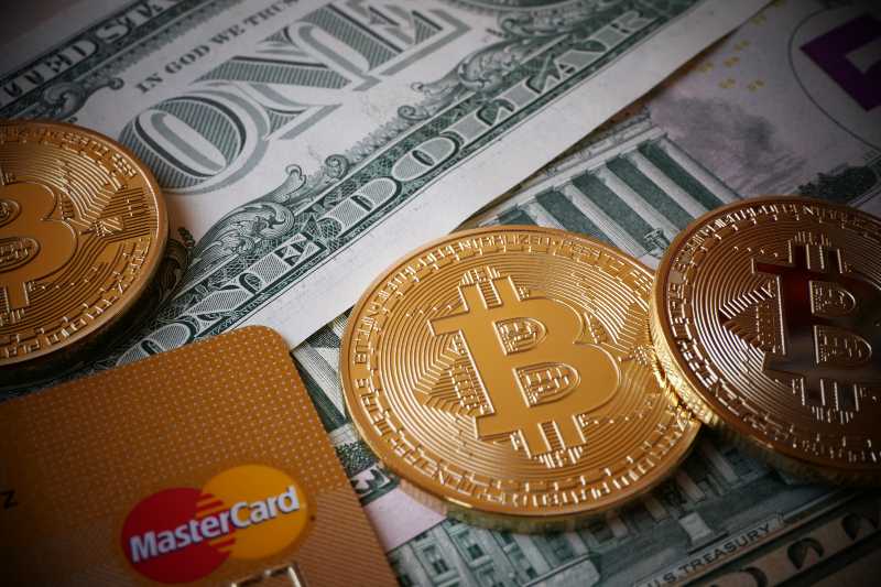 Bitcoins, an virtual currency in physical form, displayed on US-Dollars notes and a MasterCard credit card-Crypto Services