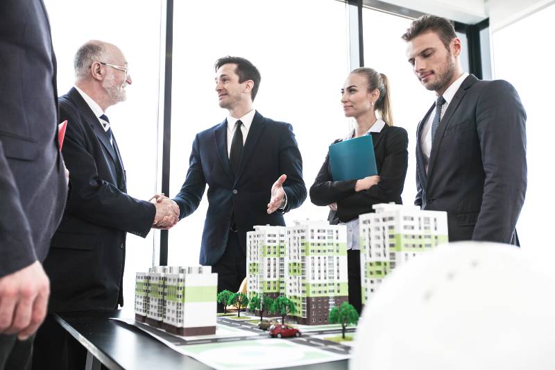 Business people standing near residential quarter houses models and shaking hands-Real Estate Investor