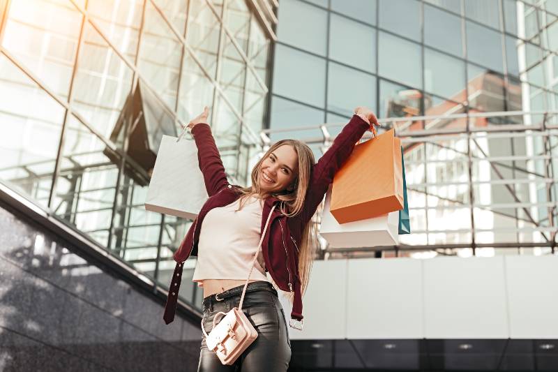 From below of content young stylish female shopaholic in trendy outfit holding shopping bags-Consumer Confidence