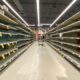 Shelf at a supermarket mostly empty with only a few packages of toilet paper left | Americans may face empty shelves | featured