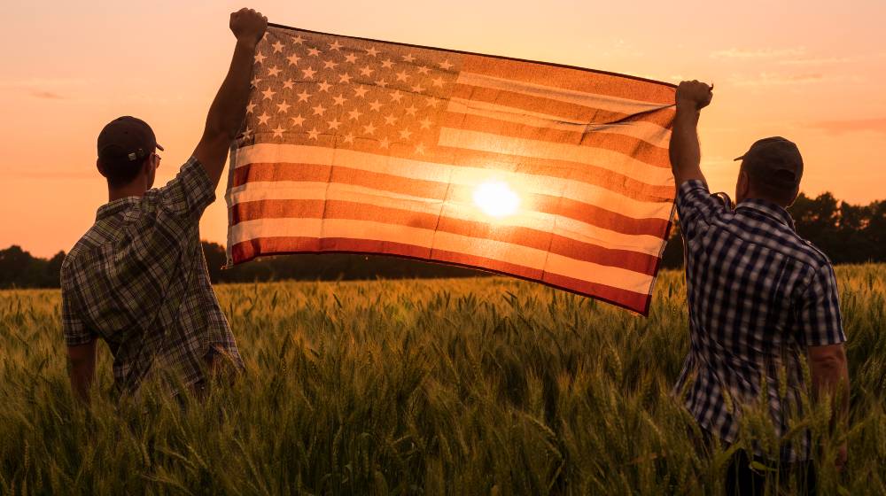 Two men energetically raised the US flag in a picturesque field of wheat | COVID-19 Kills Twice More Rural Americans Vs City Folk | featured