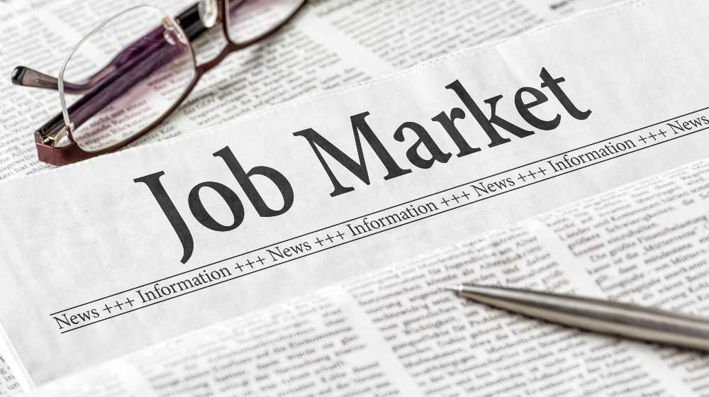 A newspaper with the headline Job Market | US Unemployment Claims Fall To Lowest Levels in 20 Months | featured