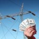 Hand holding US dollar bills in front of a high voltage power lines | Biden Signs $1 Trillion Infrastructure Bill Into Law | featured