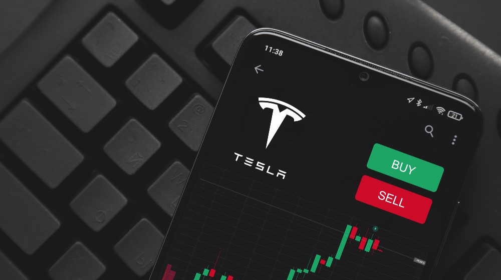 Logo Tesla on screen smartphone | Elon Musk Faces $15b Tax Bill as He Plans to Sell Tesla Stock | featured