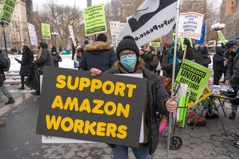 Protestors hold signs and march on a picket line across from Amazon's Whole Foods Market-Amazon Workers