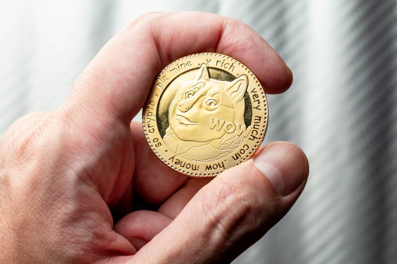Golden Dogecoin token coin in a caucasian male hand | Dogecoin Over Bitcoin