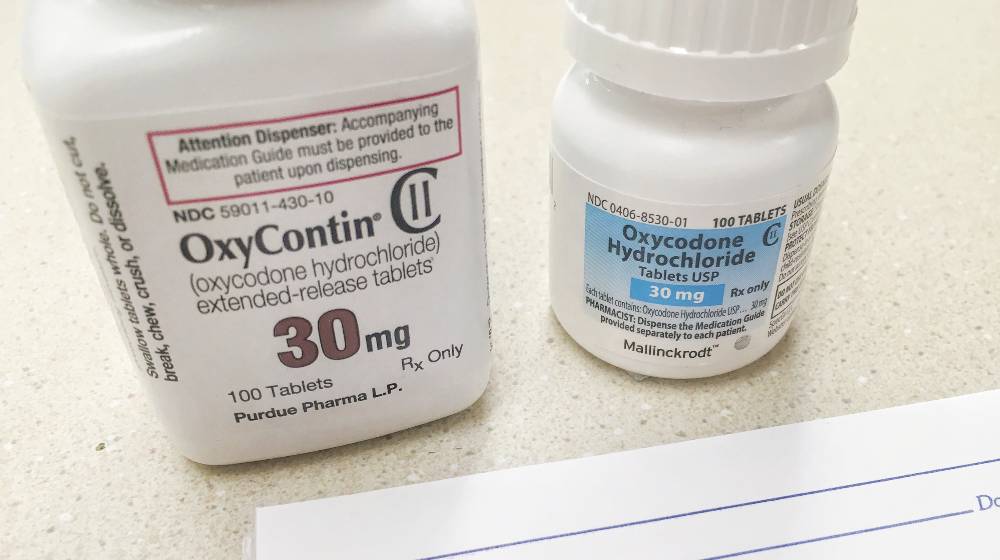 OxyContin and oxycodone bottle on counter with rx prescription pad | Judge Junks Oxycontin Settlement, Orders Sackler Family to Pay Up | featured