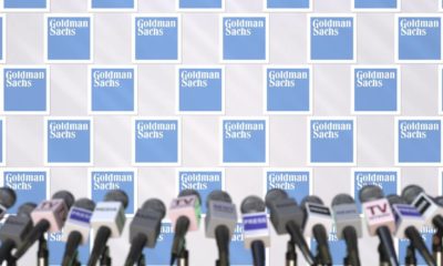 Press conference of goldman sachs, press wall with logo and microphones | Goldman Sachs Cut GDP Forecast After Manchin’s Says No To BBB | featured