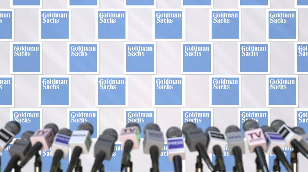 Press conference of goldman sachs, press wall with logo and microphones | Goldman Sachs Cut GDP Forecast After Manchin’s Says No To BBB | featured