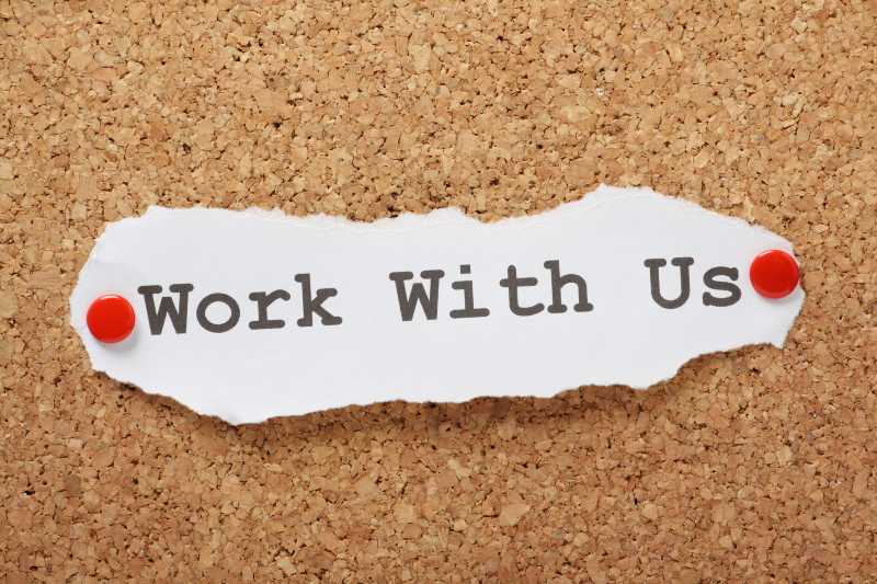 The phrase Work With Us typed on a piece of paper and pinned to a cork notice board | US Job Openings