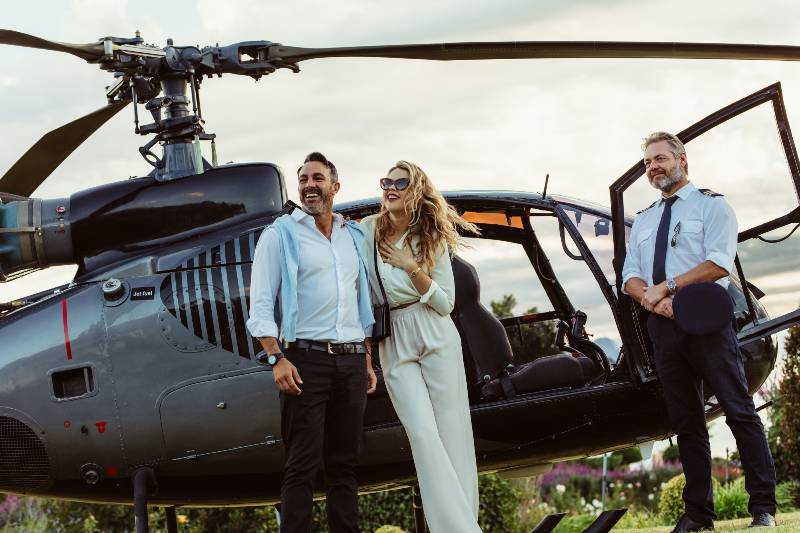 Beautiful couple alighted from a private helicopter and looking at a view with pilot standing by | Finance Friday: How to Hit $10M Net Worth in 10 Years (Or Less)