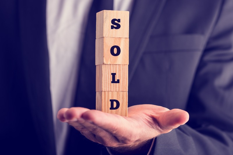Businessman holding a sold sign composed of stacked wooden blocks | AJ Patel