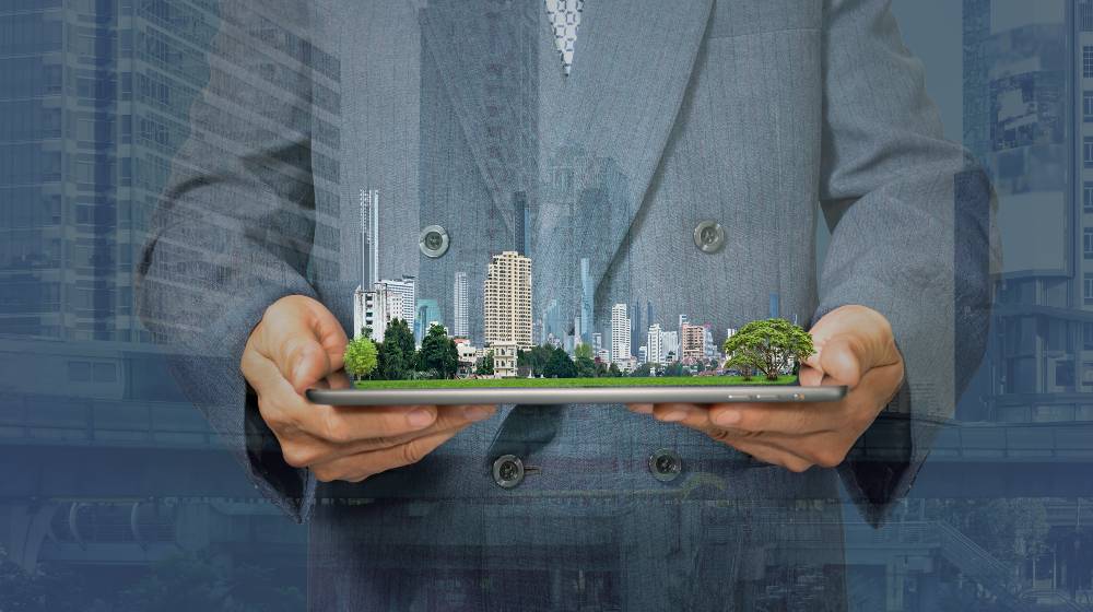 Double exposure with businessman holding tablet and city model in hands | Investors Are Buying Virtual Land Using Millions of Real Money | featured