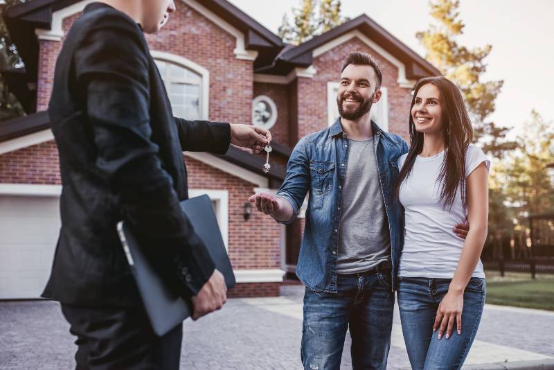 Happy couple is taking keys from their new house from broker and smiling | Home Buyers