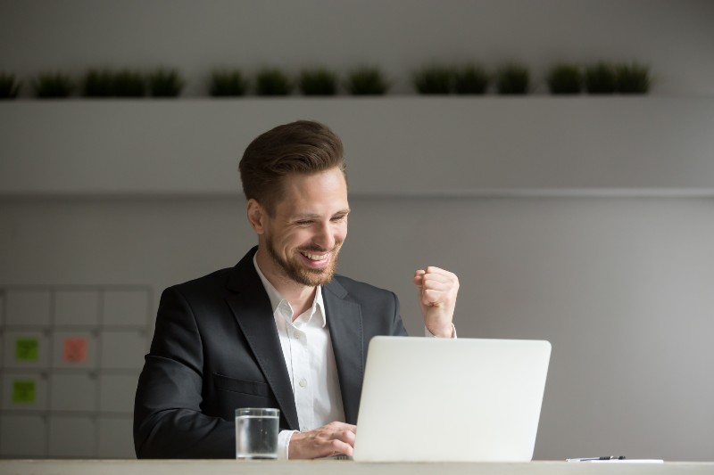 Happy young businessman in suit looking at laptop excited by good news online | jacob