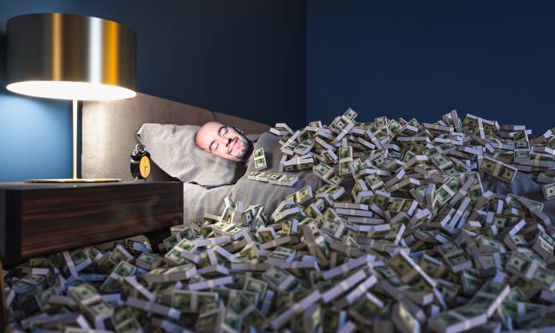 Smiling man sleeping in a bed covered with dollars money. wealth concept | Three Habits You Must Develop To Become Wealthy