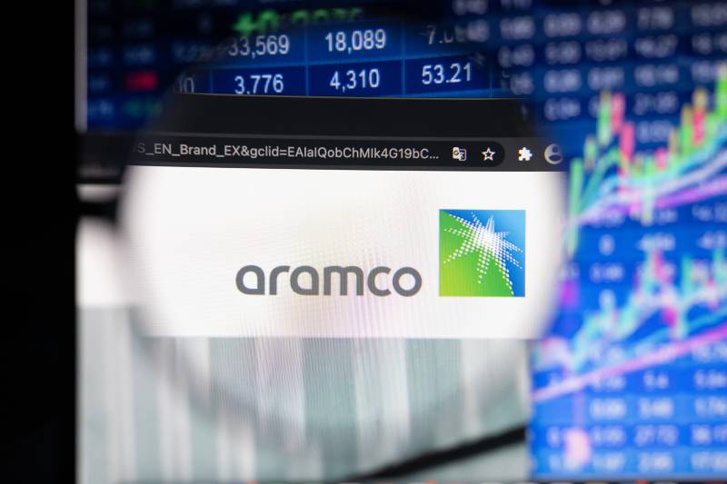 Aramco company logo on a website with blurry stock market developments in the background | Saudi Aramco Posts $110 Billion In Net Income