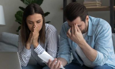 Young married couple sit on couch at home calculating expenses feel upset | US Household Expenses Are Now Higher By $296 Per Month | featured
