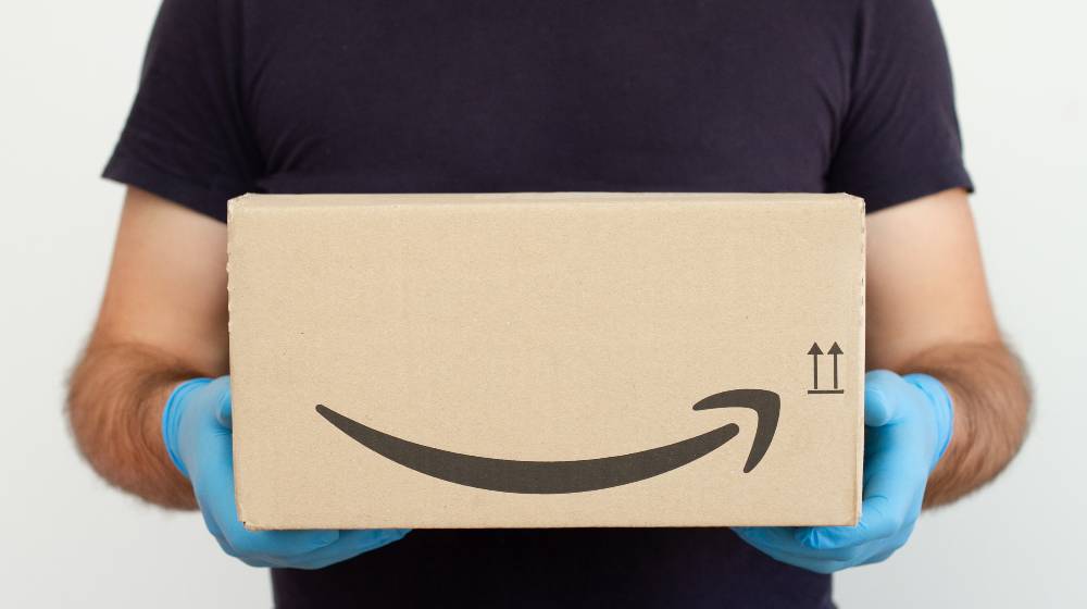 Amazon Delivery. Delivery man holding cardboard boxes in medical rubber gloves | LinkedIn Says Amazon Is The Best Company To Work for in 2022 | featured