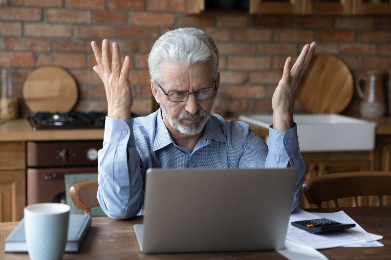 Annoyed worried aged man pensioner sit by laptop unable to make utility bill loan payment | Soaring Inflation is Wrecking Retiree Pensions
