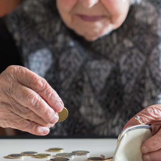 Elderly 95 years old woman sitting miserably at the table at home and counting remaining coins from the pension | Retiree Pensions Losing Value As Inflation Continues to Soar | featured