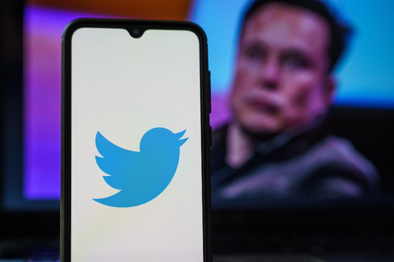 Twitter logo on smartphone and Elon Musk in the background | Musk Buys Twitter At Nearly 40% Premium 